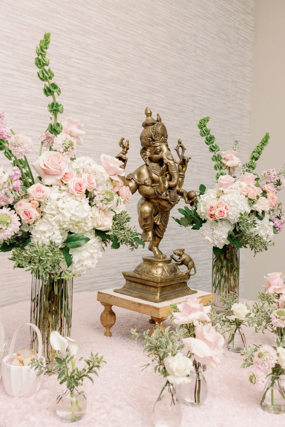 Elegant floral centerpieces with pink roses and greenery in glass vases alongside decorative brass sculptures on a white surface.