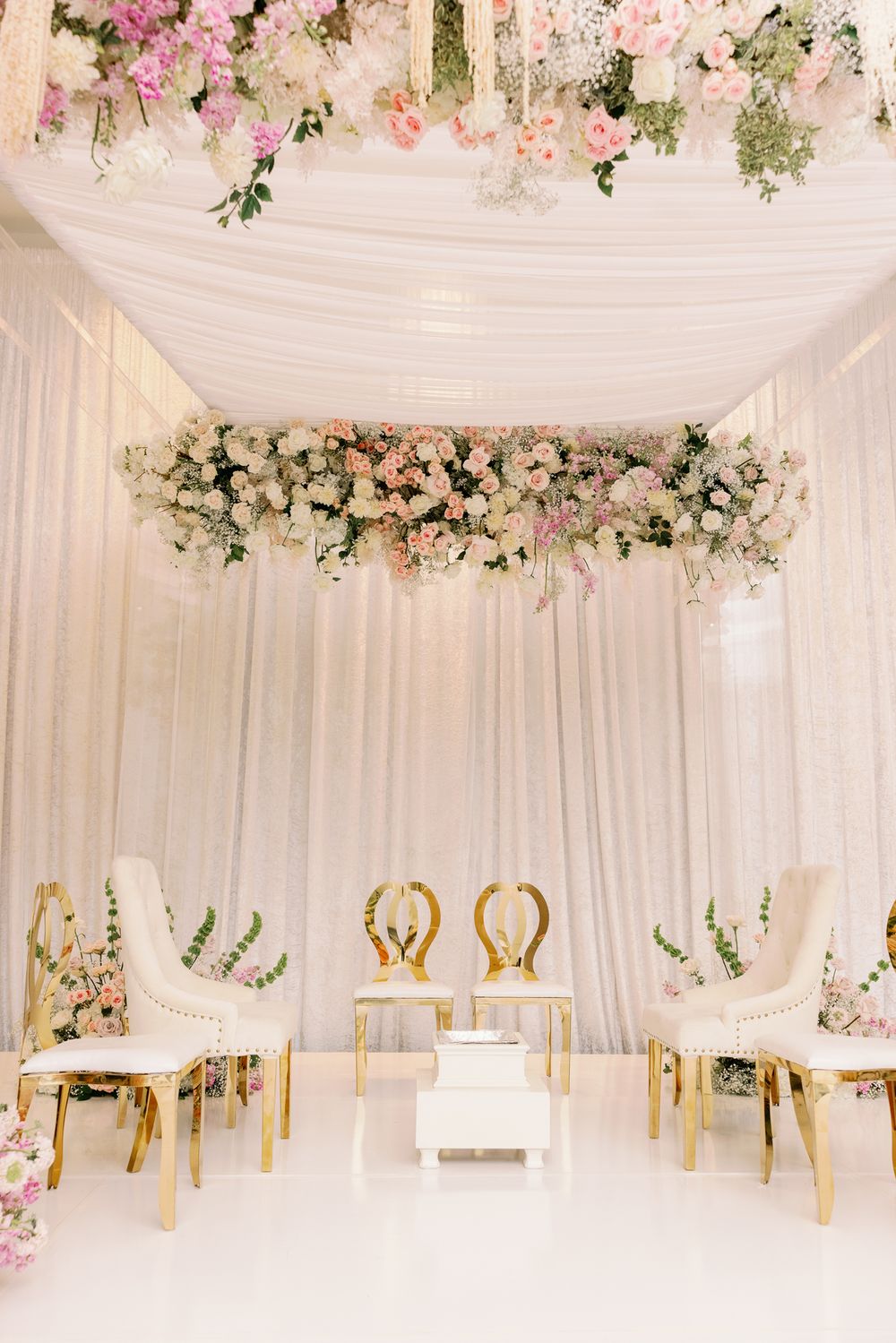 Elegant white draped wedding tent interior decorated with pink floral arrangements and gold accents for a luxurious reception.