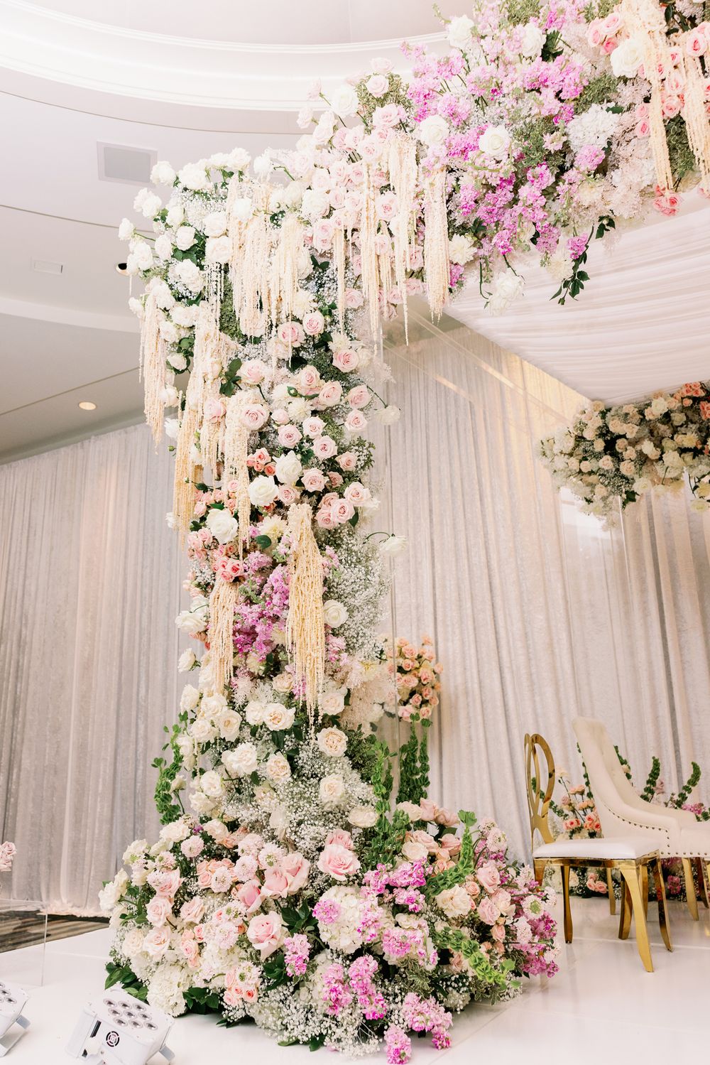 Elegant wedding venue decorated with cascading pink and white floral arrangements against white draped walls.