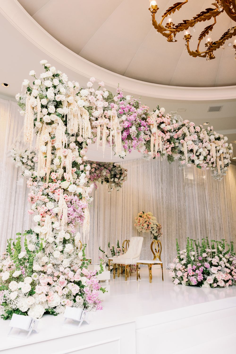 Elegant white wedding backdrop with cascading floral arrangements and crystal chandeliers creating a romantic atmosphere.