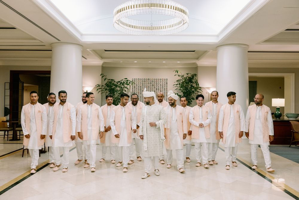 A group of people wearing matching cream-colored traditional Indian wedding attire stand together in an elegant hotel lobby.