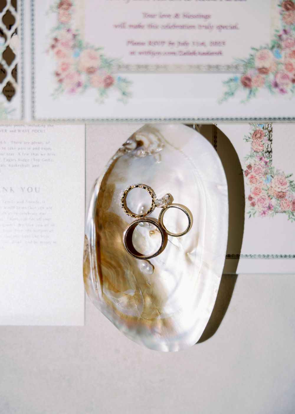 Wedding rings artistically photographed on mother of pearl surface with floral invitation details.
