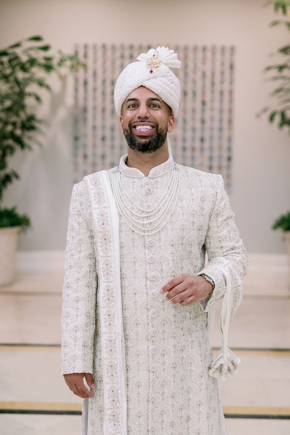 A traditional Indian groom poses in an elegant white embroidered sherwani and matching turban during a wedding photoshoot.