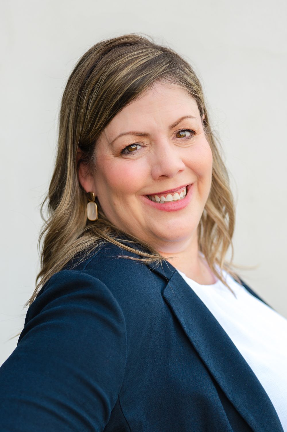 Professional headshot series showing warm smiles and expressions against a light background while wearing a navy blazer.