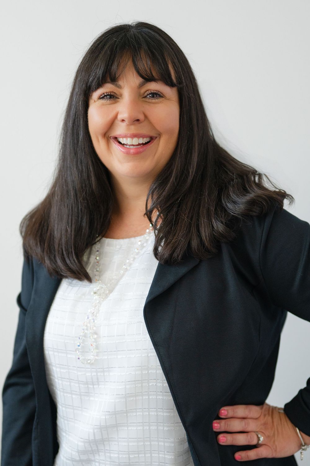 Business portraits featuring someone in a black blazer and white lace top with dark bangs against a white backdrop.