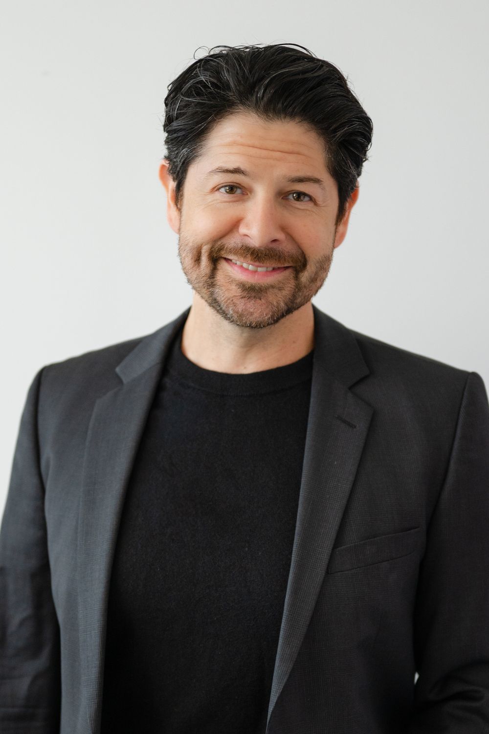 Professional headshots of a man in a dark blazer and sweater smiling against a white background.