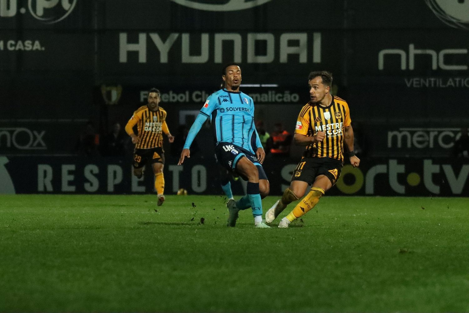 Soccer match action shows players from opposing teams battling for control on a nighttime field.