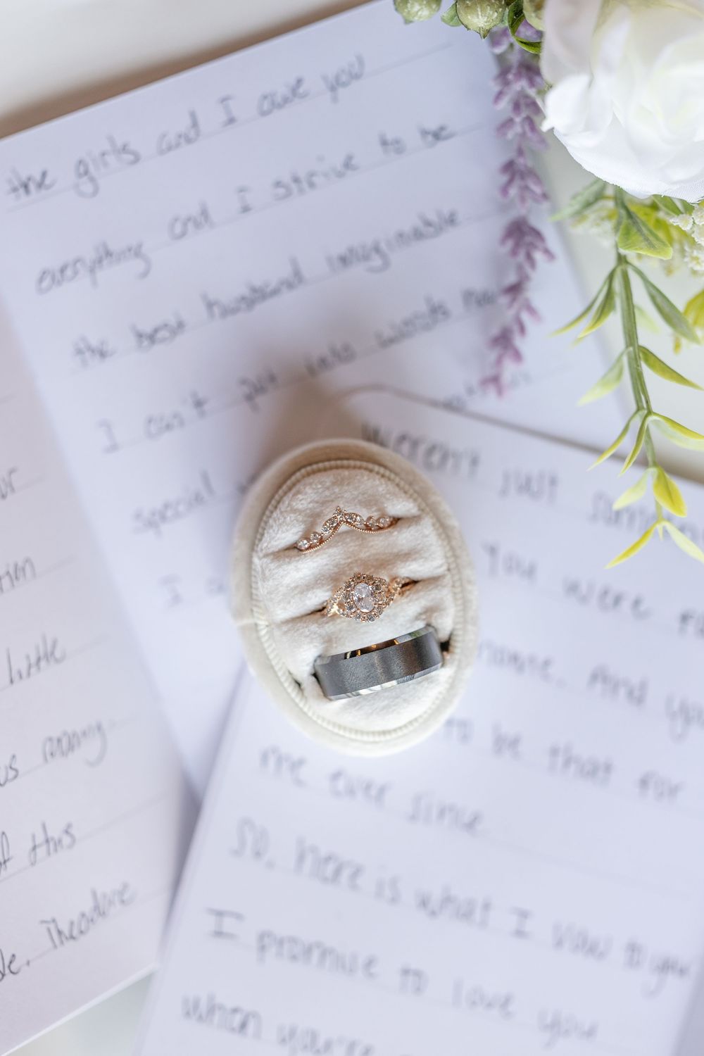Wedding rings displayed on a white cushion with handwritten vows and floral decorations.