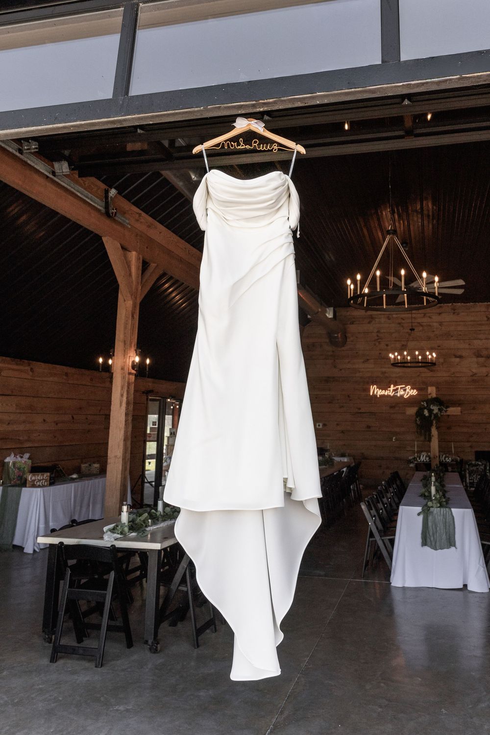 White wedding dress hanging in a rustic wooden reception venue with round tables.
