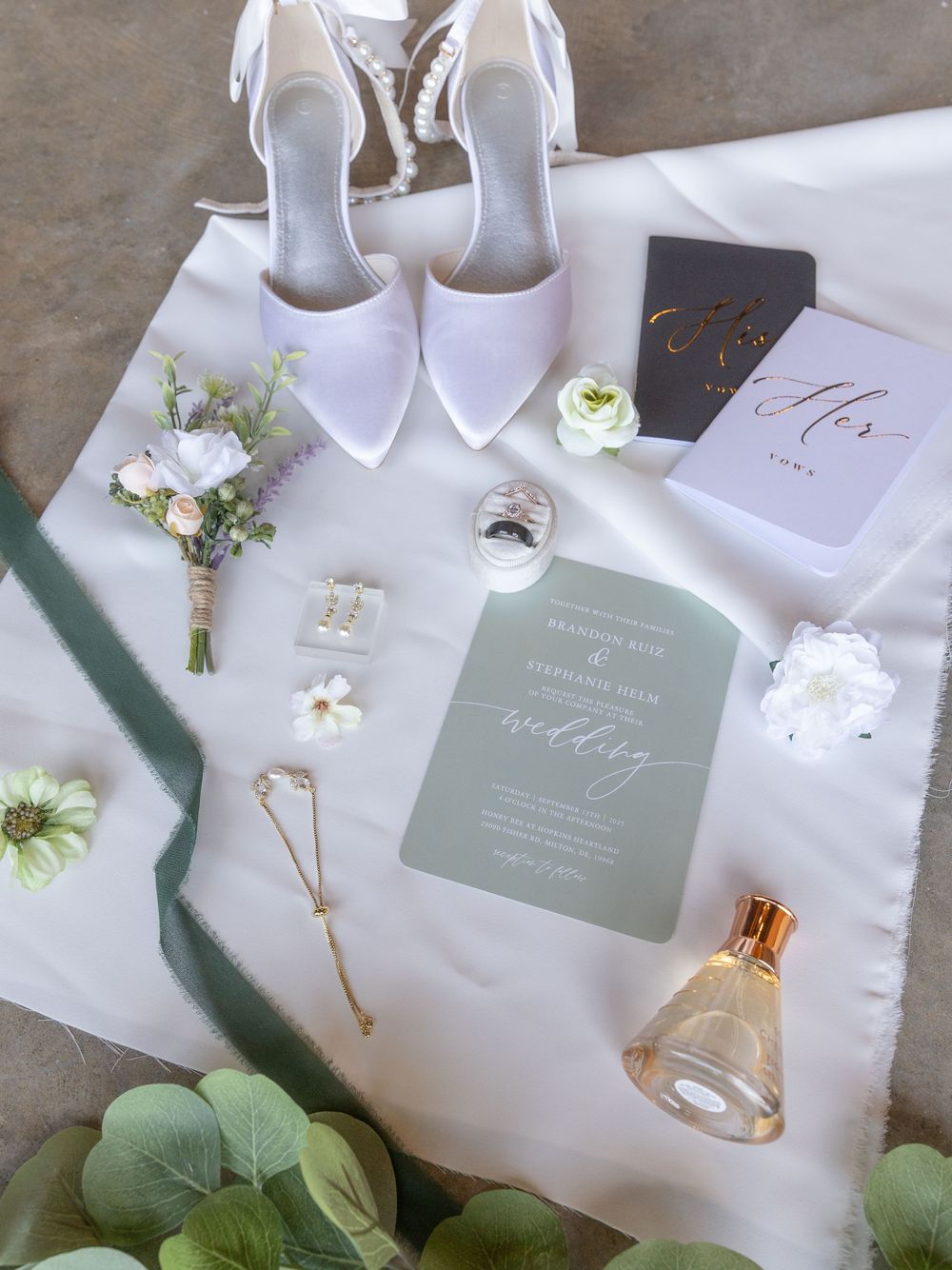 Wedding accessories including white shoes, invitations, and floral details arranged on a white surface.