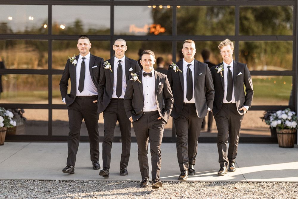 Groomsmen in black suits walking together outdoors at a wedding venue.