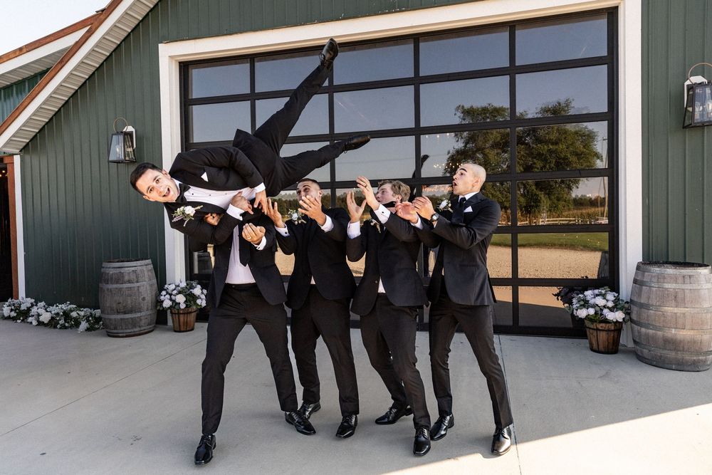 Wedding party members jumping and celebrating outside a modern barn venue.