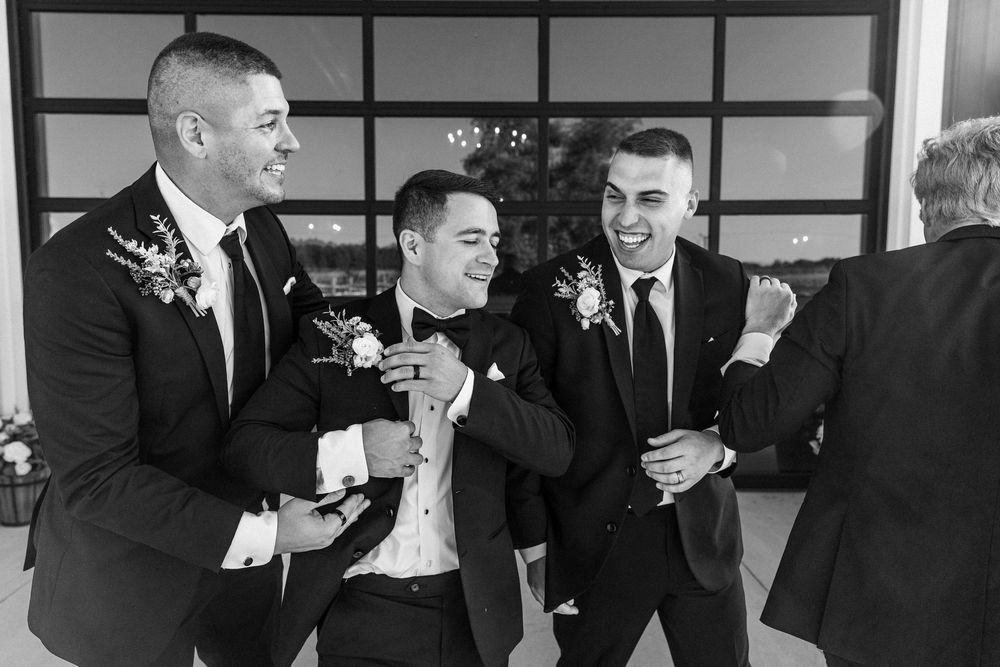 Black and white photo of groomsmen sharing laughs and drinks during wedding celebrations.