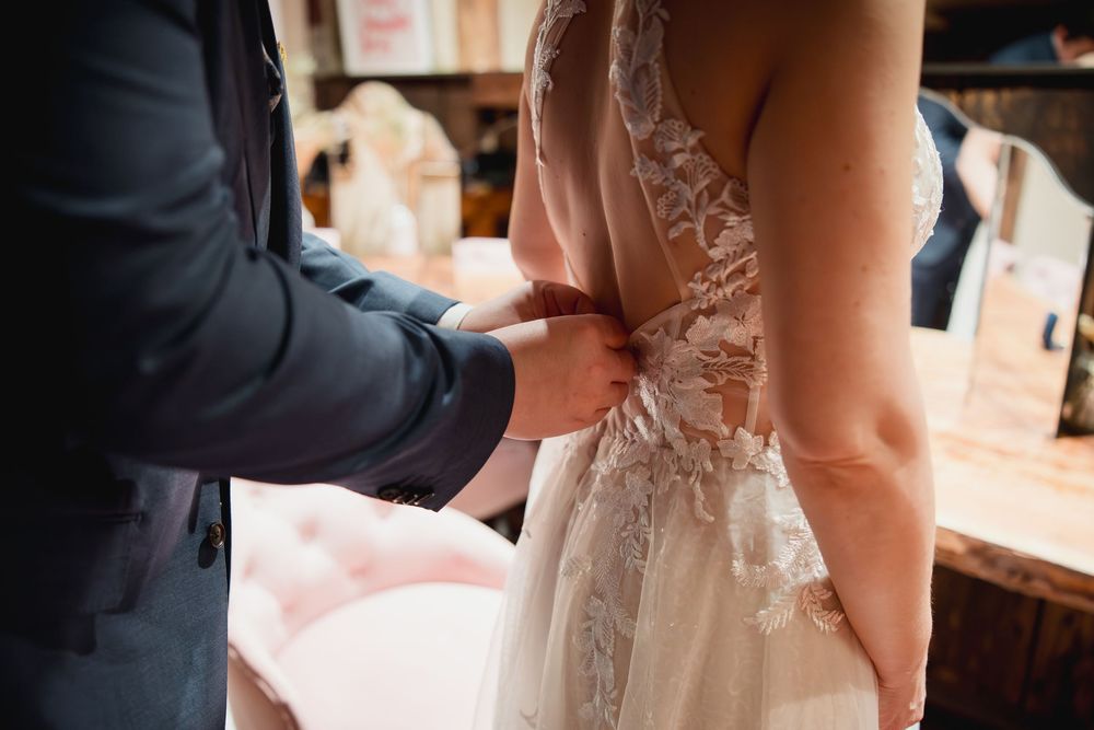 A close-up view of a wedding dress being adjusted, showing intricate lace details and delicate buttons on the back.