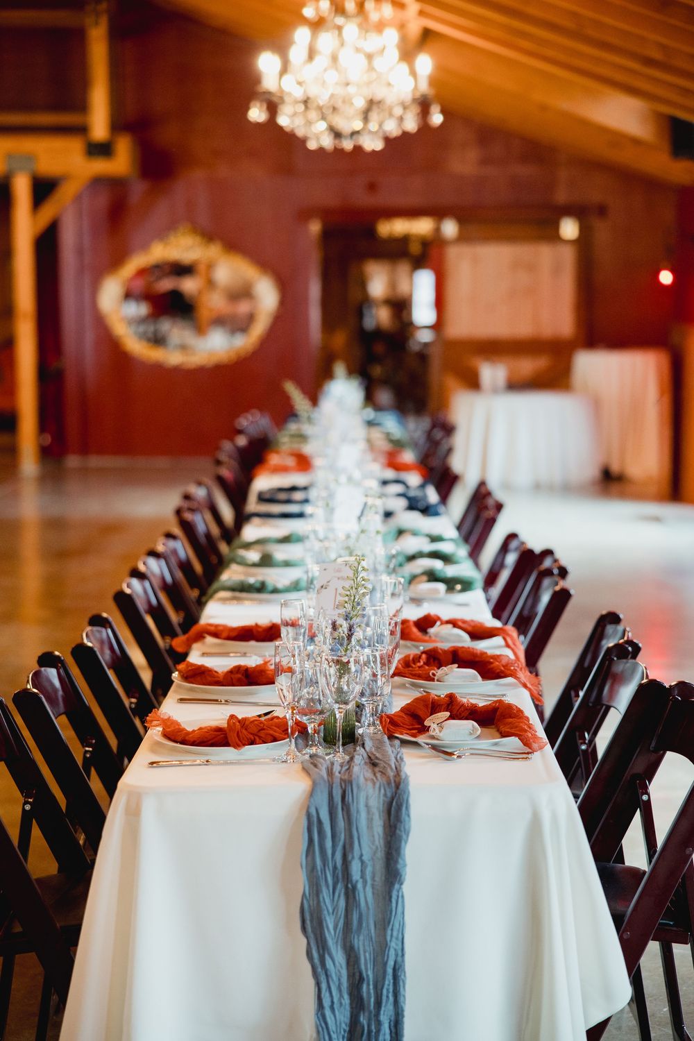 Elegant wedding reception tables set with white linens, red napkins and crystal chandeliers in a grand ballroom.