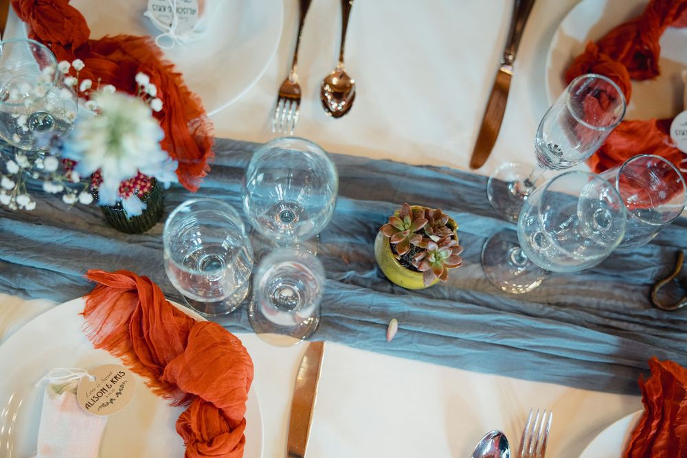 Elegant wedding reception table settings with burnt orange napkins and crystal glassware on a rustic wooden surface.