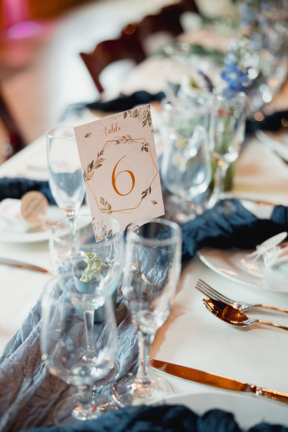 Elegant table settings with ornate table number cards and glassware at a formal event.