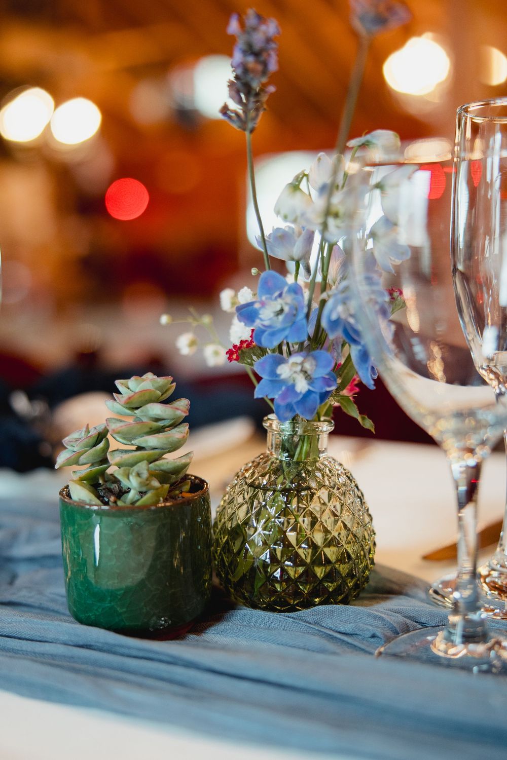 Elegant table setting with small potted succulents and blue flowers in green vessels as centerpiece decorations.