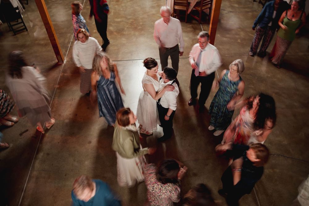 Wedding guests dance together on a rustic wooden floor during a lively reception celebration.