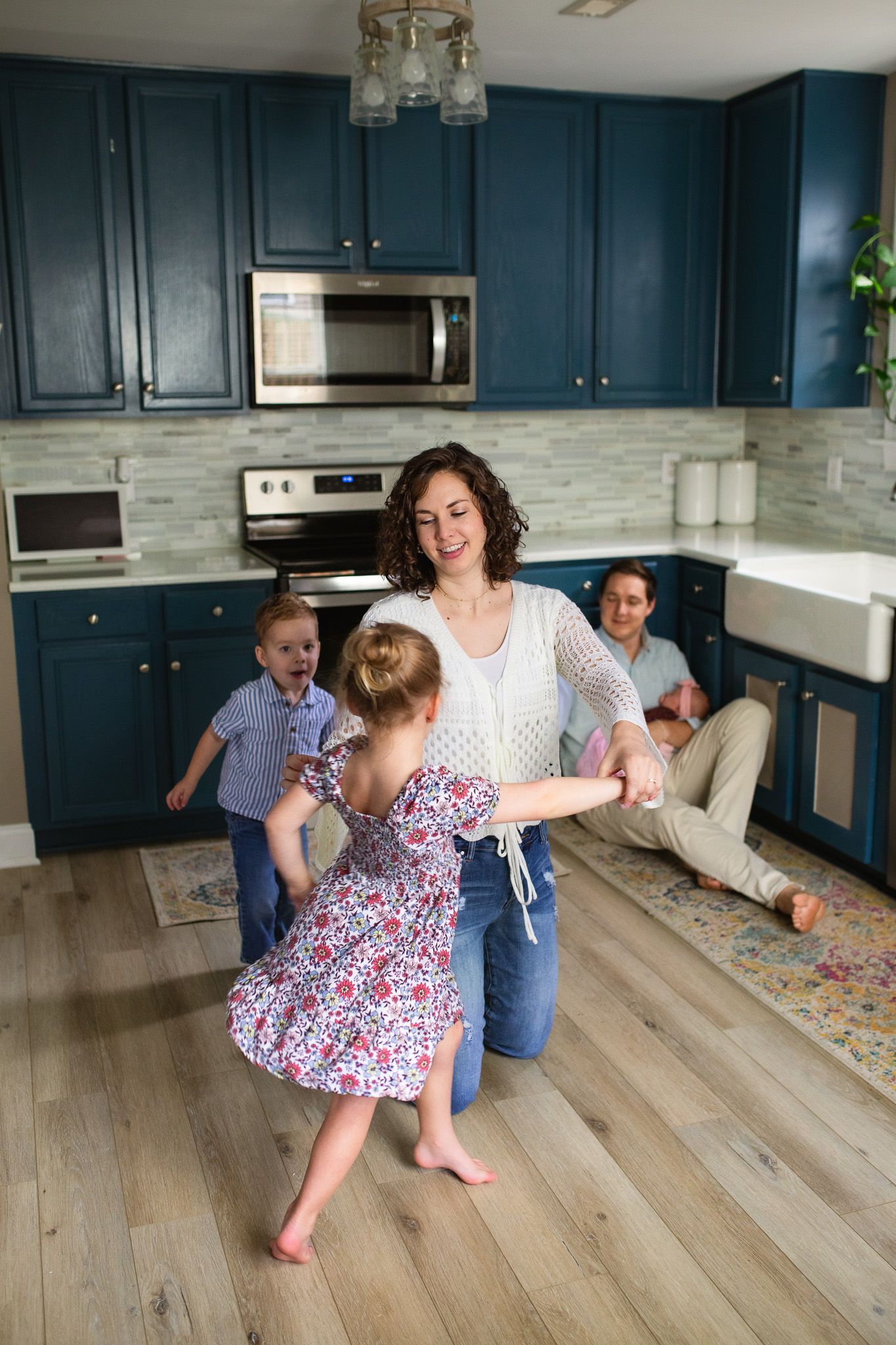 A family dances together in a modern kitchen with blue cabinets and light wood floors.