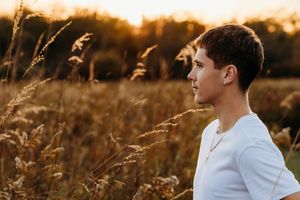 A person in a white shirt stands in a golden field at sunset with tall grass swaying in the warm light.