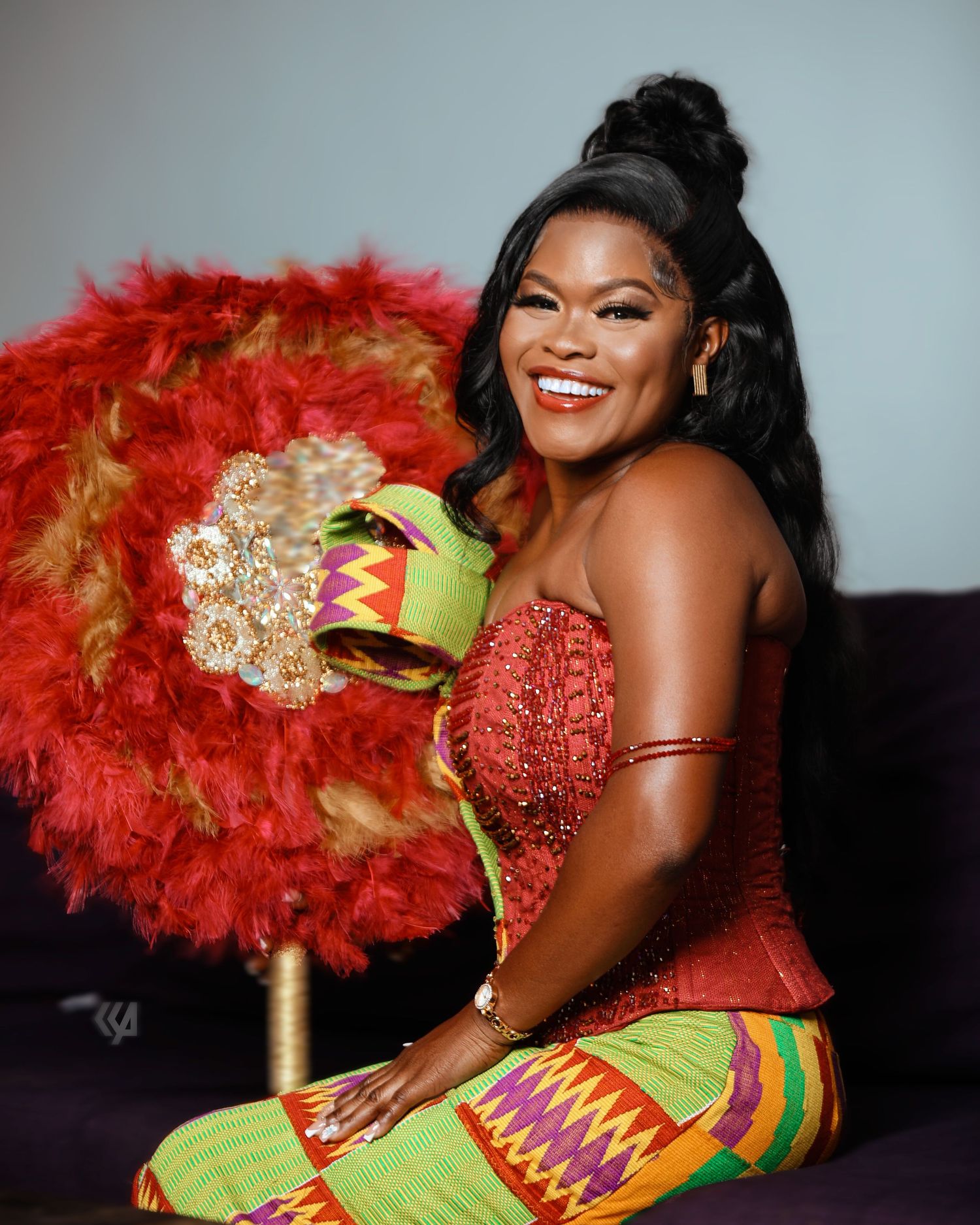 A festive portrait session featuring traditional African attire with vibrant red feathers and green kente cloth details.