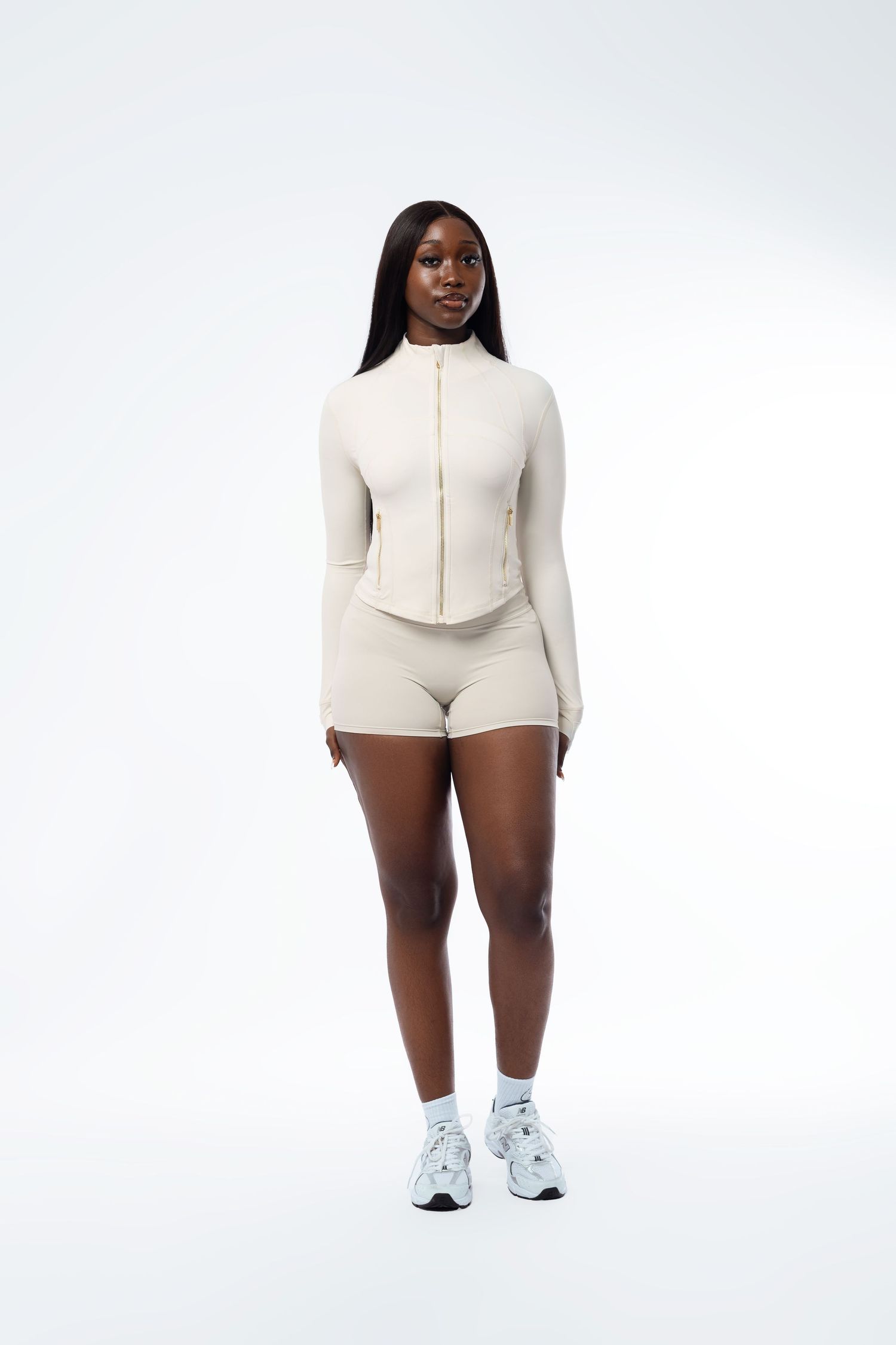 Model in white zippered activewear set poses against minimalist background.