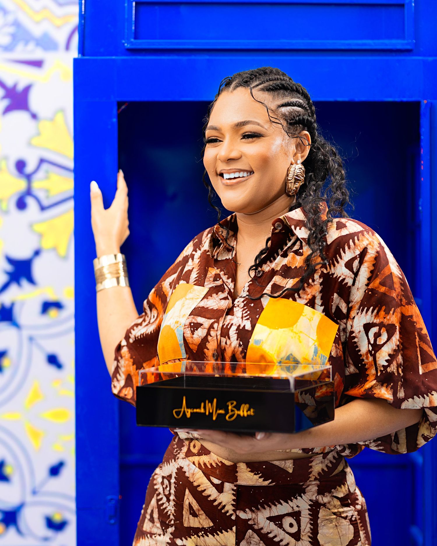 Model in brown patterned dress poses energetically against bright blue backdrop with stars.