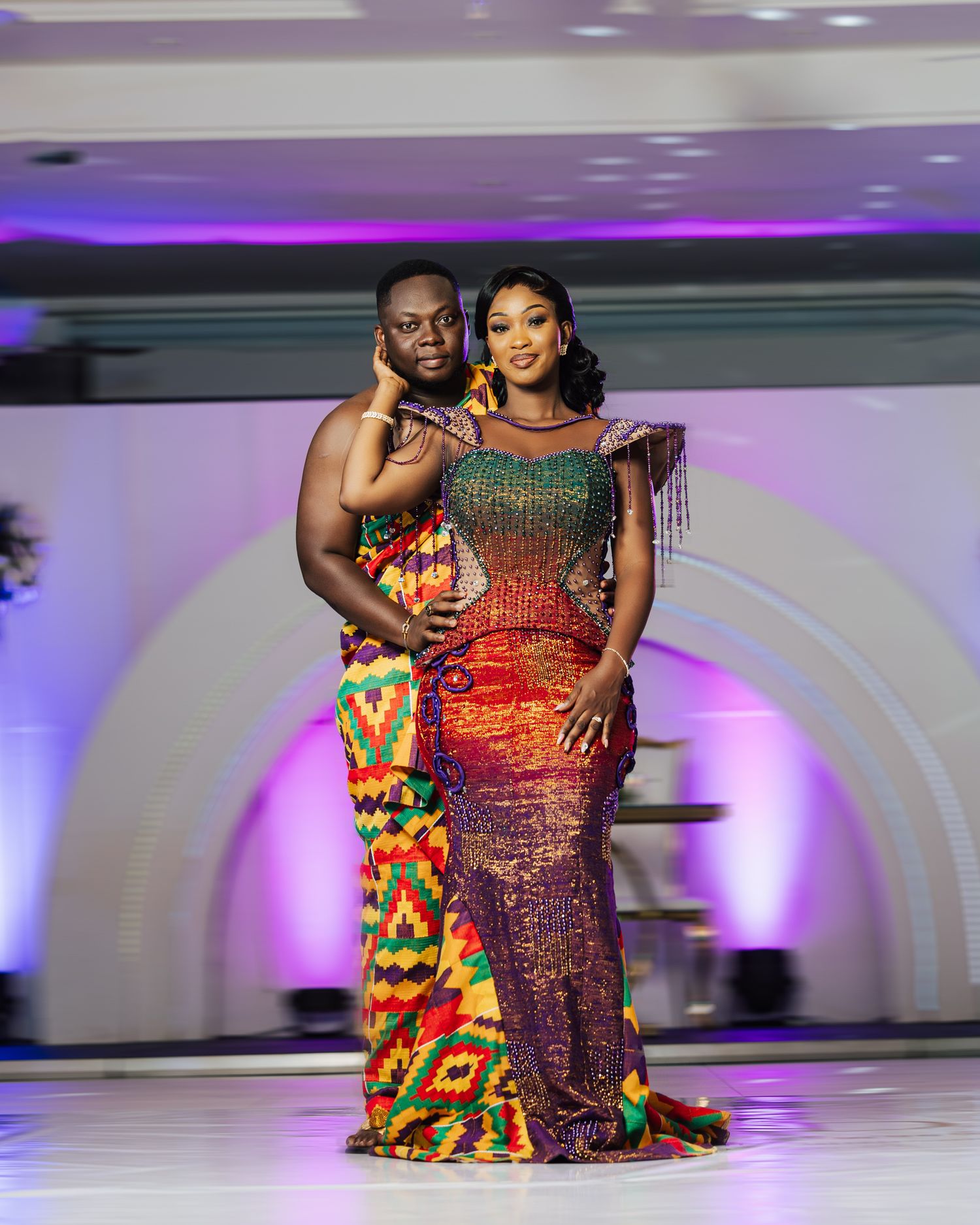 A couple poses in traditional African formal wear featuring vibrant patterns and beaded details.
