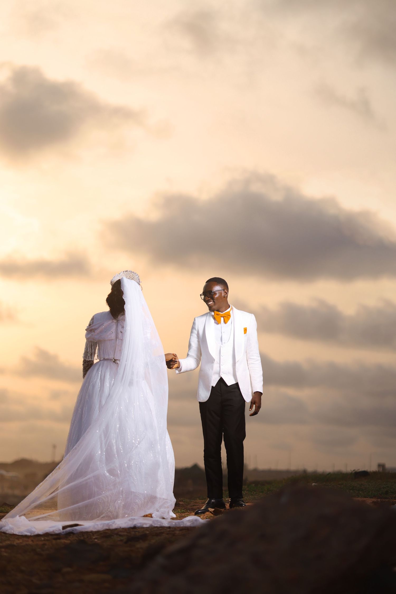 A wedding couple poses on a hilltop during golden hour with flowing white dress and formal attire.
