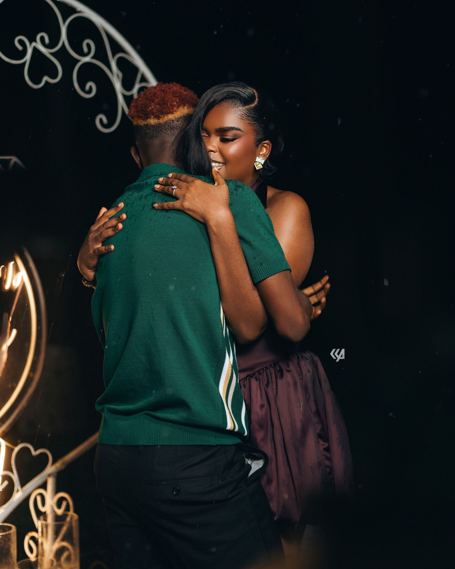 A couple shares a warm embrace while dancing, the woman wearing a maroon dress and the man in a green shirt.