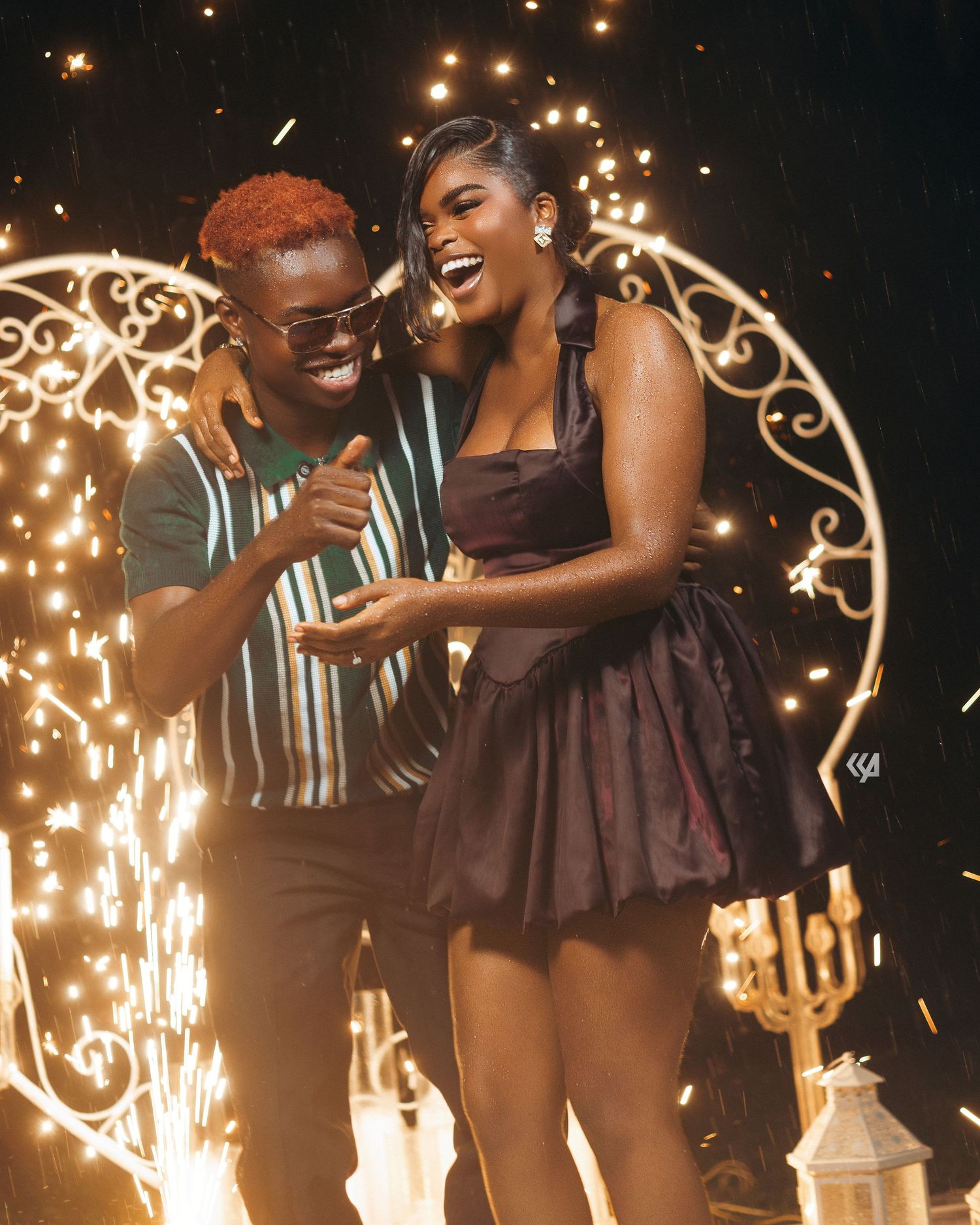 Two joyful people laughing together at a sparkling celebration event, woman in purple mini dress and man in striped shirt.