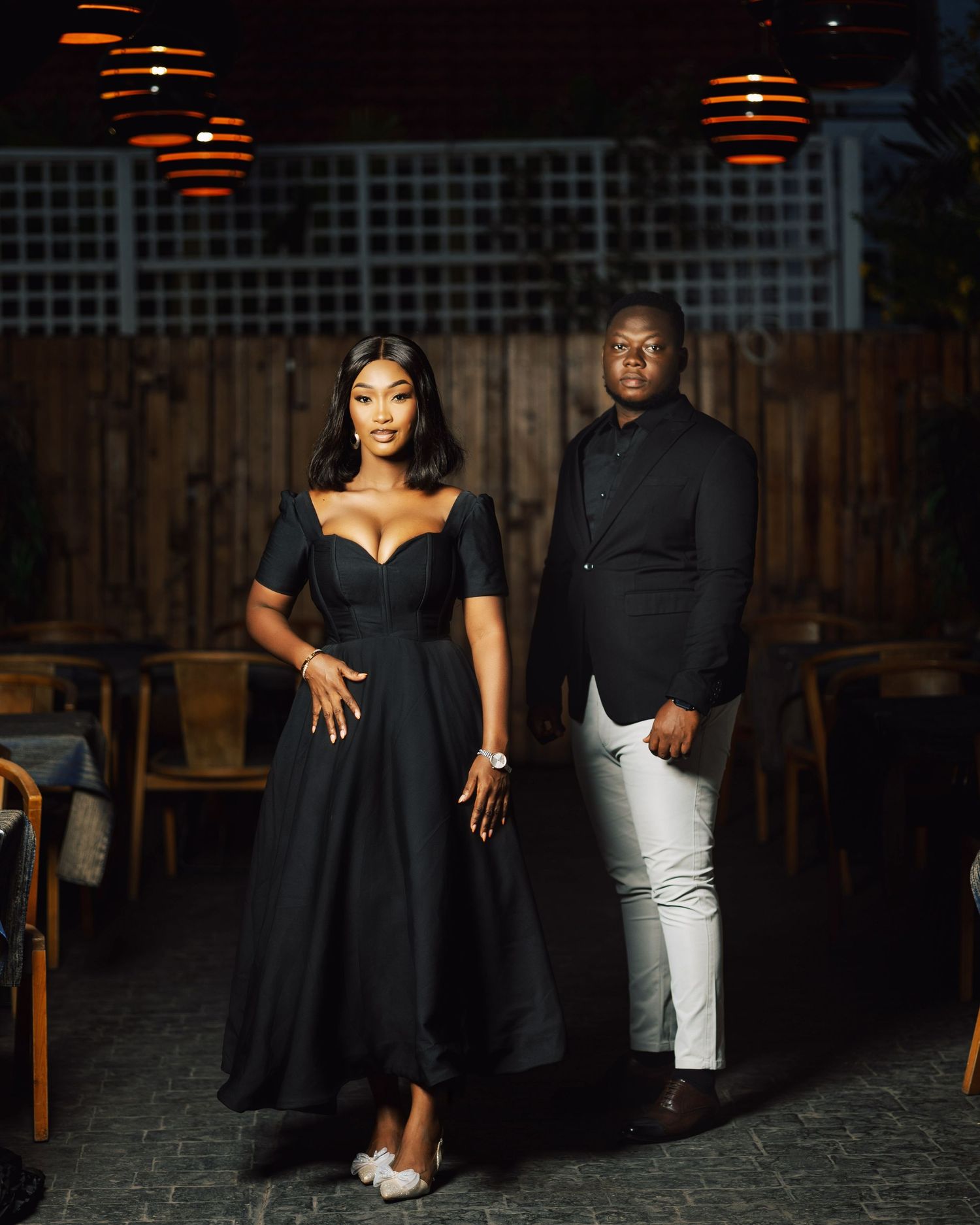 Stylish couple's photoshoot in black attire at a dimly lit restaurant setting.