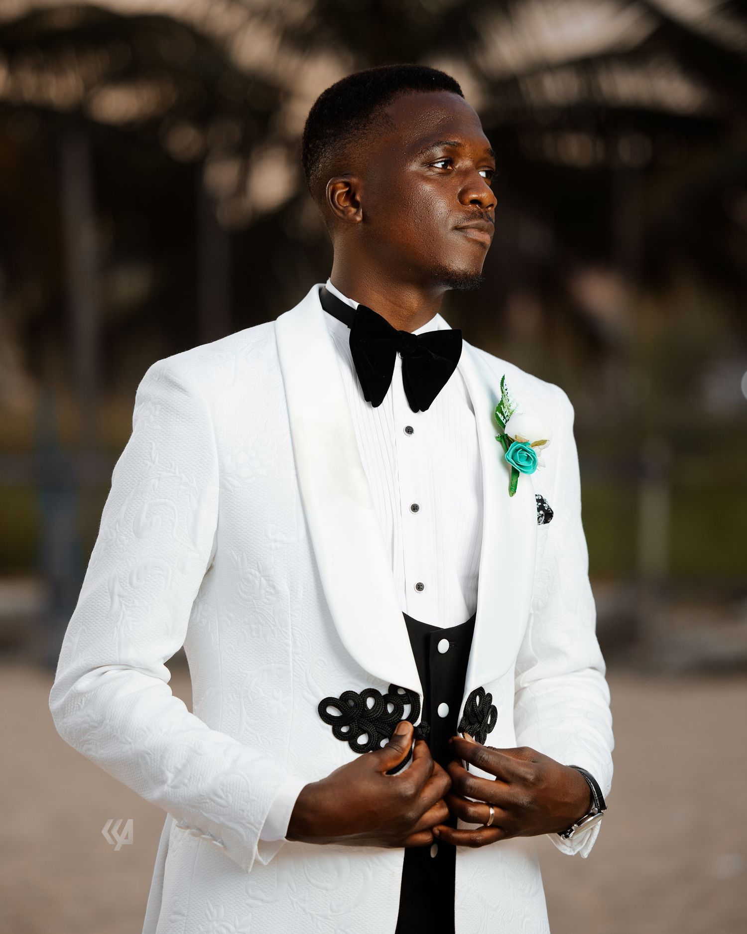 A groom in a classic white tuxedo with black bow tie and floral boutonniere.