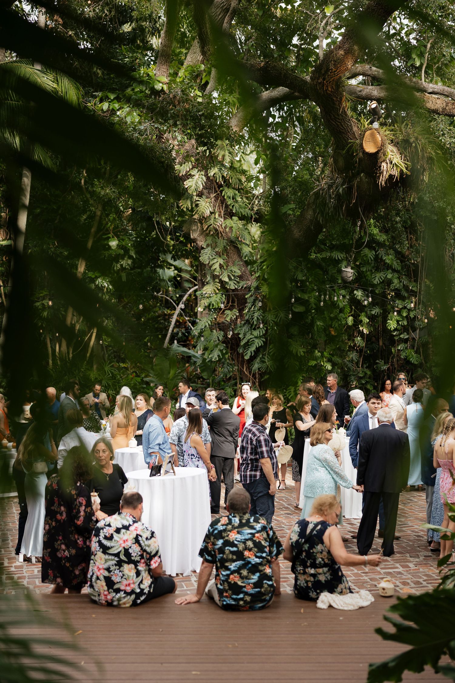 A group of people gathered at an outdoor event on a wooden deck surrounded by lush greenery and trees.