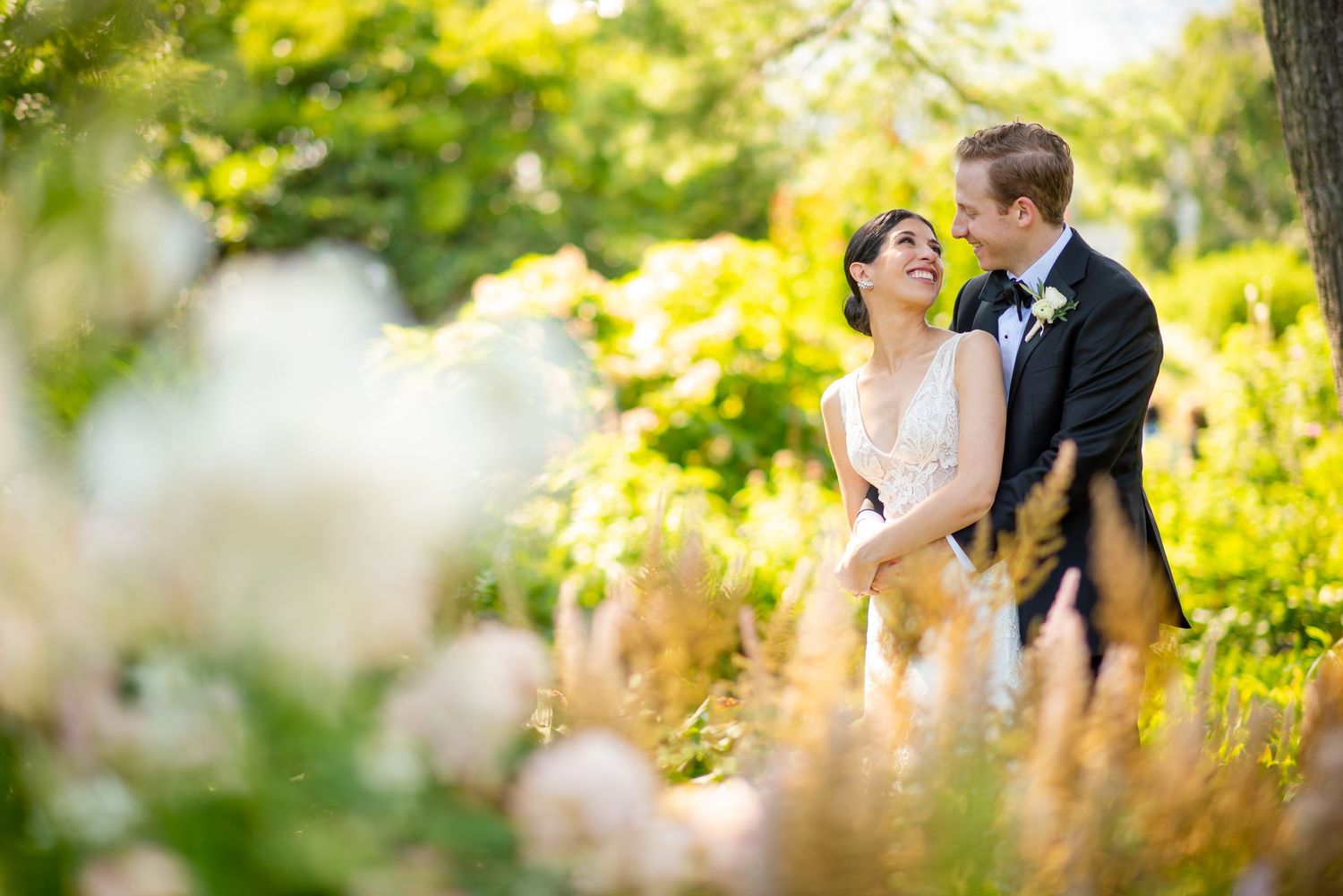 A couple in wedding attire stands amidst soft yellow foliage during an outdoor photo session.
