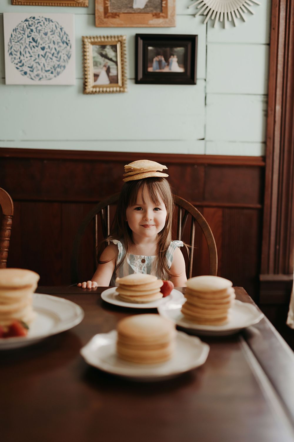 Stack of fluffy pancakes on white plate at restaurant table with rustic wood paneling and wall decor in background.