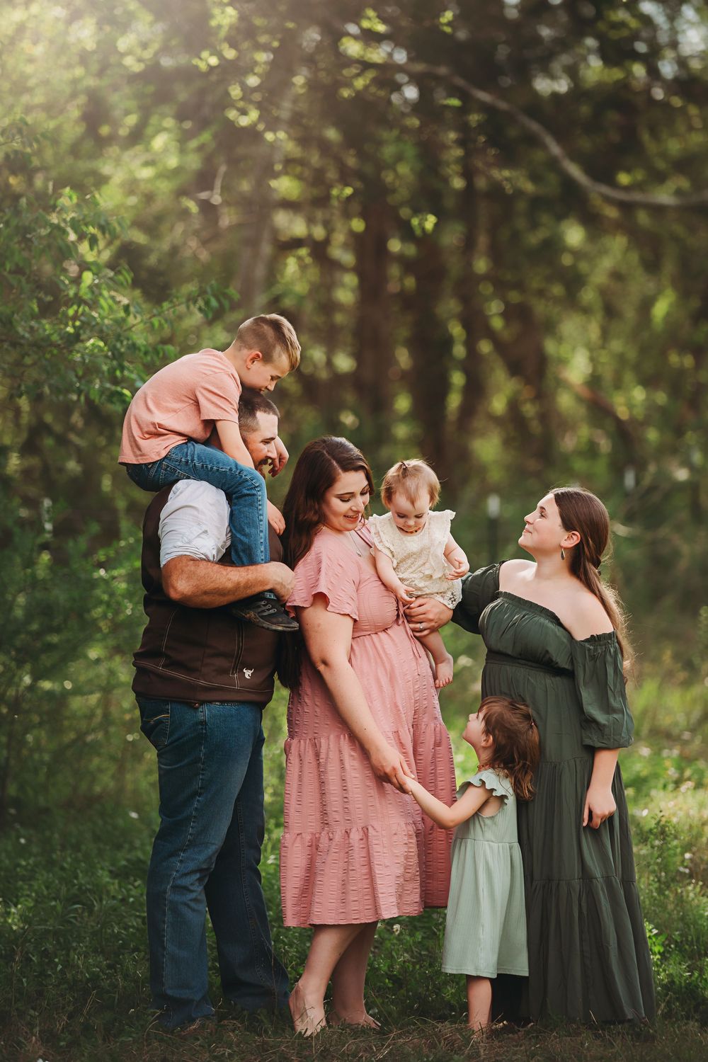 Family of four shares tender moments together in a sunlit forest setting wearing coordinated pink and green outfits.