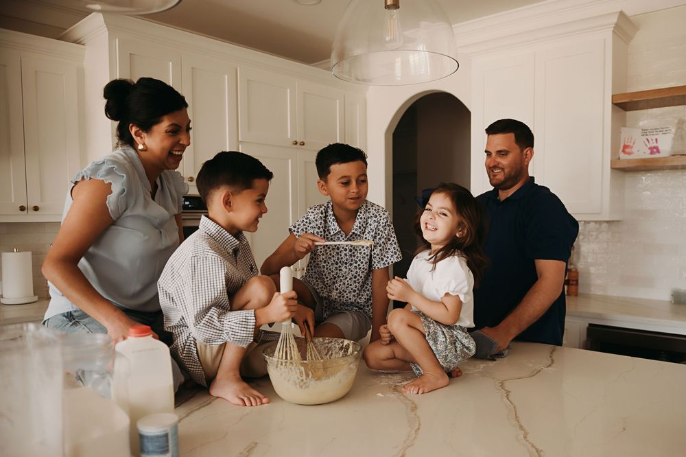 Family members gather around a white kitchen counter to prepare food together.