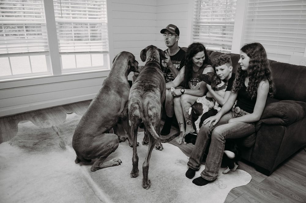 A series of black and white photos showing people relaxing on couches with their dogs in various casual poses.
