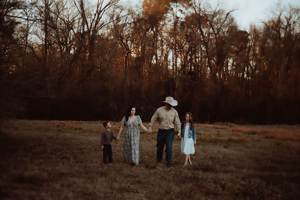 A group walks through a sunlit autumn field at golden hour as trees create a dark silhouette in the background.