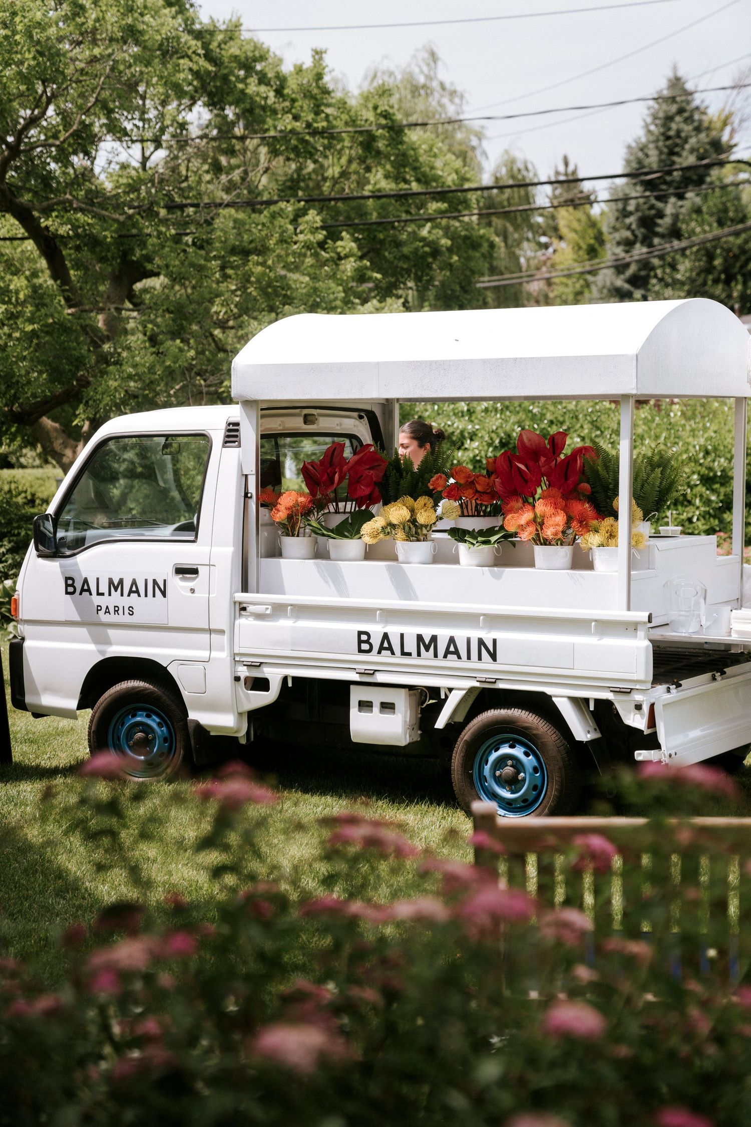 White Balmain-branded vintage truck decorated with vibrant red and orange flowers for an outdoor event display.