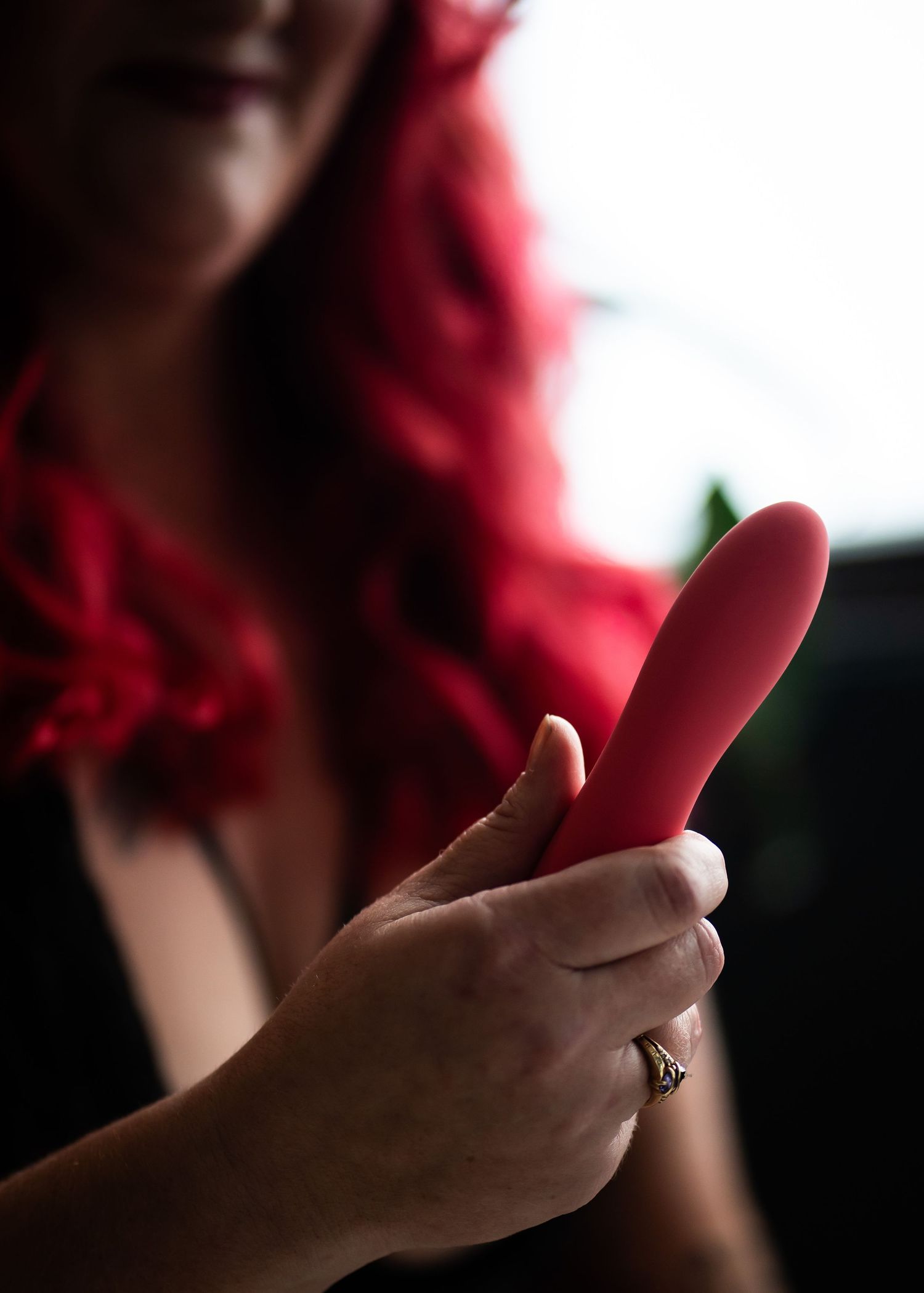 A hand holding a pink vibrator toy against a dark background with red blurred elements in the frame.