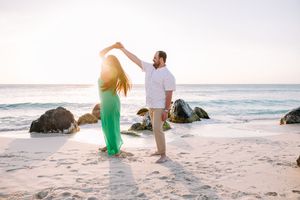 Romantic beach photoshoot with couple in white and green outfits at sunset.