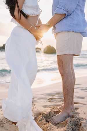 Close up of couples feet standing together on sandy beach at sunset.