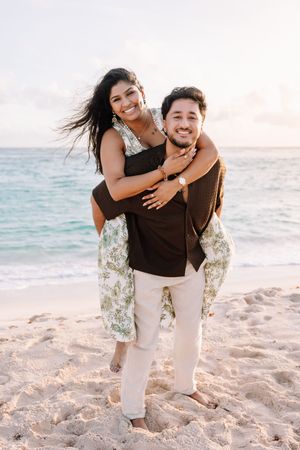 Playful couple having fun on sandy beach during sunset photoshoot.