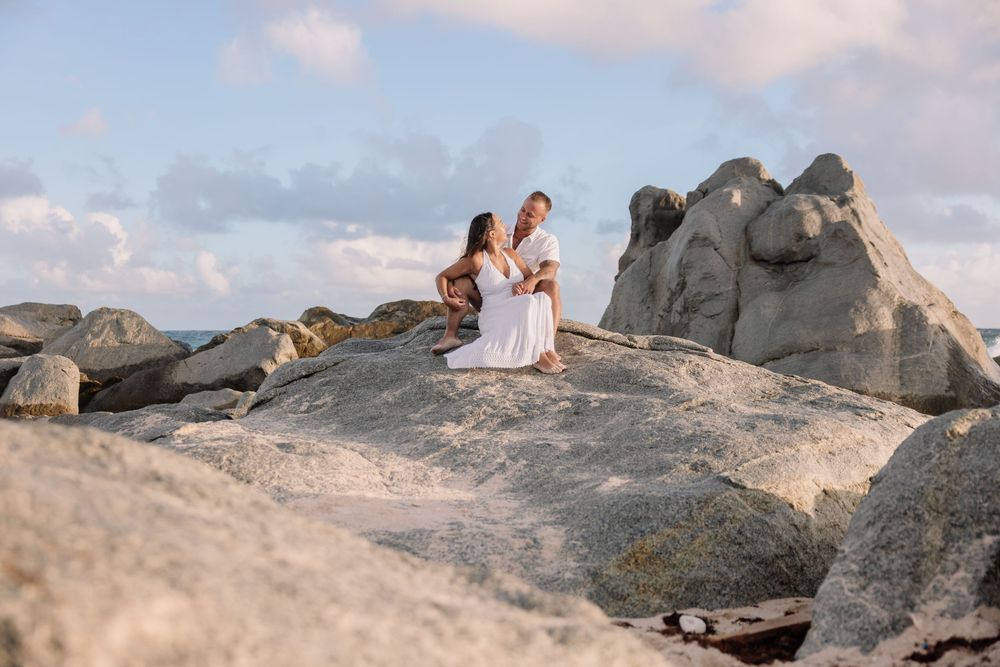 Couple sitting on rocky coastal formation during golden hour photoshoot.