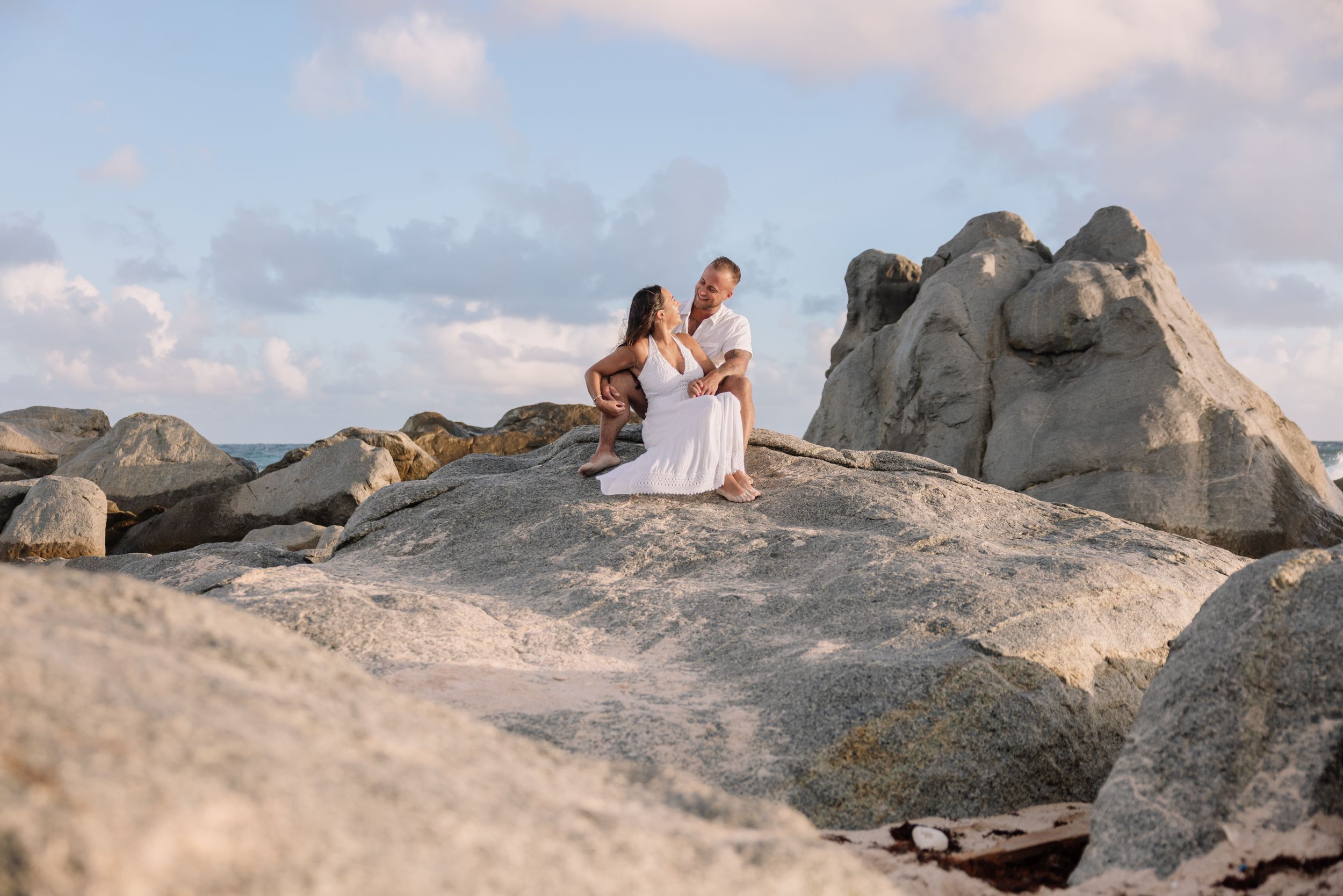 Couple sitting on rocky coastal formation during golden hour photoshoot.