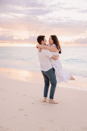 Romantic couple embracing and dancing on beach at sunset with soft pink sky.
