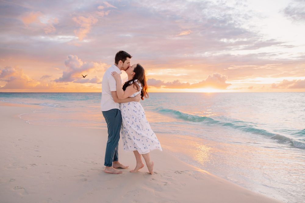 Romantic couple dancing on beach at sunset with orange and pink sky.